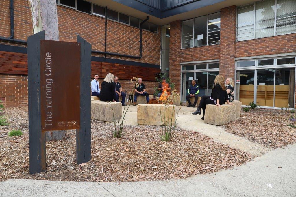 Yarning circle sign and people sitting around alight fire pit.