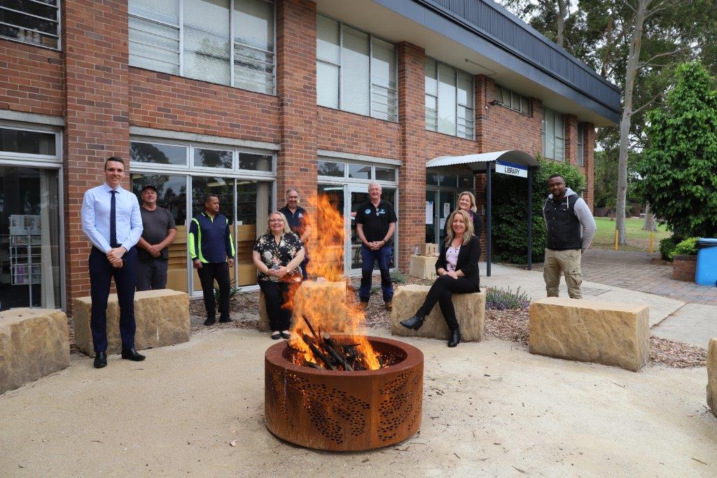 Fire pit alight with several people behind it.