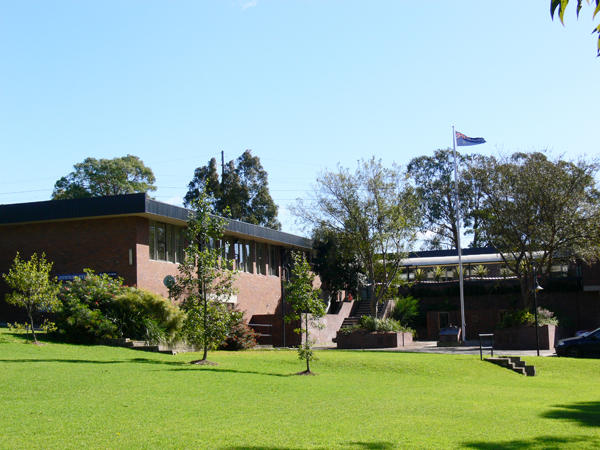 Large brick building with stairs, surrounded by cenotaph and grass area.