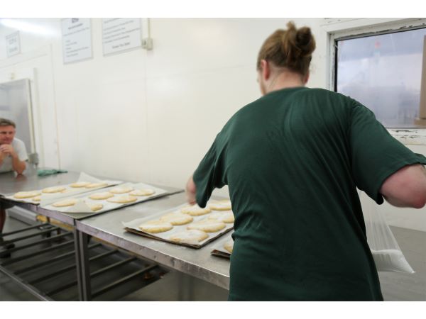 A man with hair tied back, dressed in a green t-shirt, holds a hand out over a tray of cookies