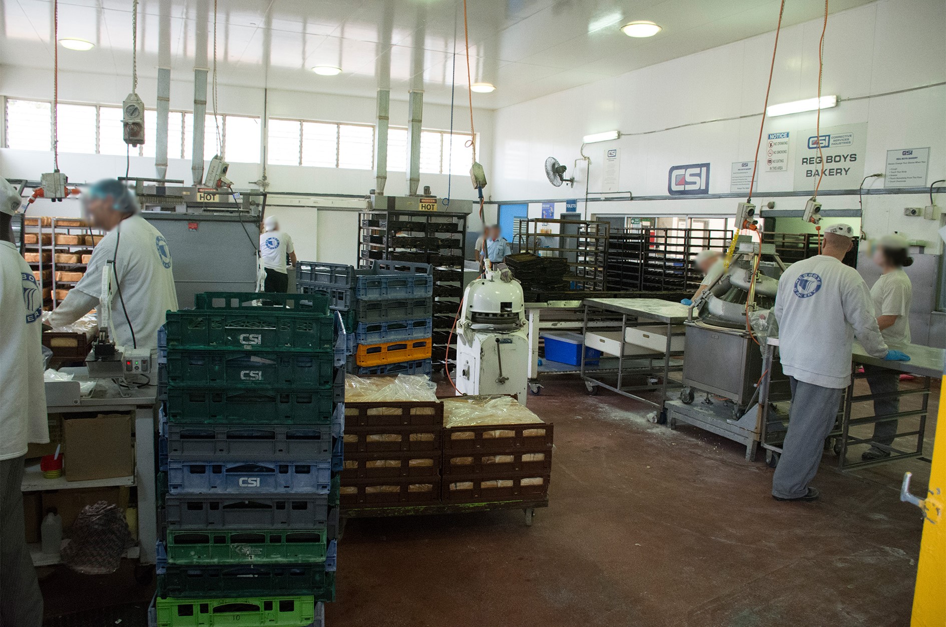 People in white chef shirts standing at different work stations in a high-ceilinged room, preparing baked goods