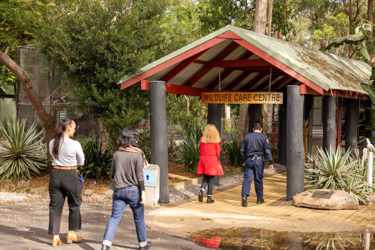 A male officer in uniform and 3 plain clothes women with long hair walking into passageway with the sign Wildlife Care Centre