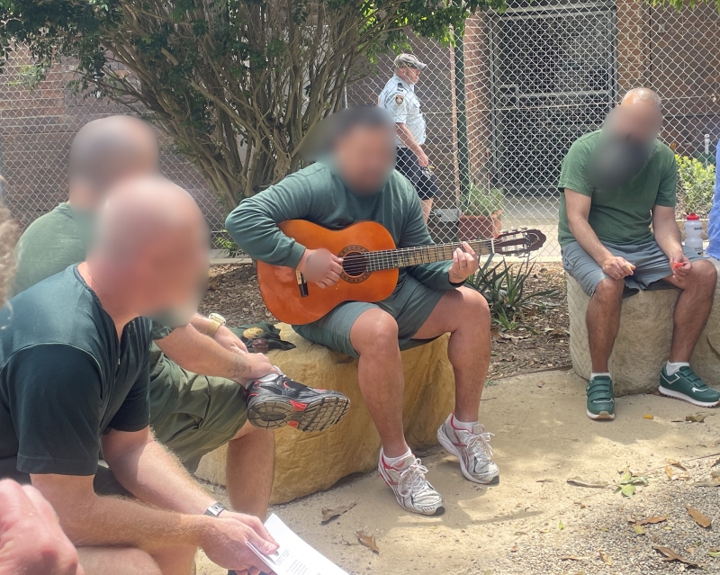 Men sitting in a circle and one is playing a guitar