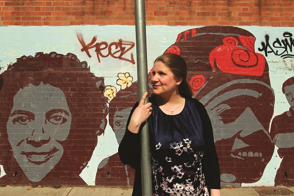 An adult female standing next to a pole looking away from the camera off into the distance