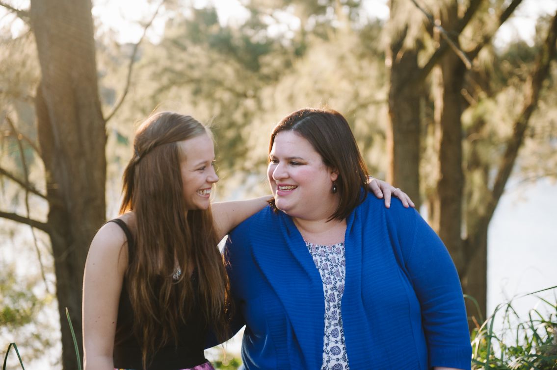 Two female adults staring at each other smiling one has her arm on the others shoulder