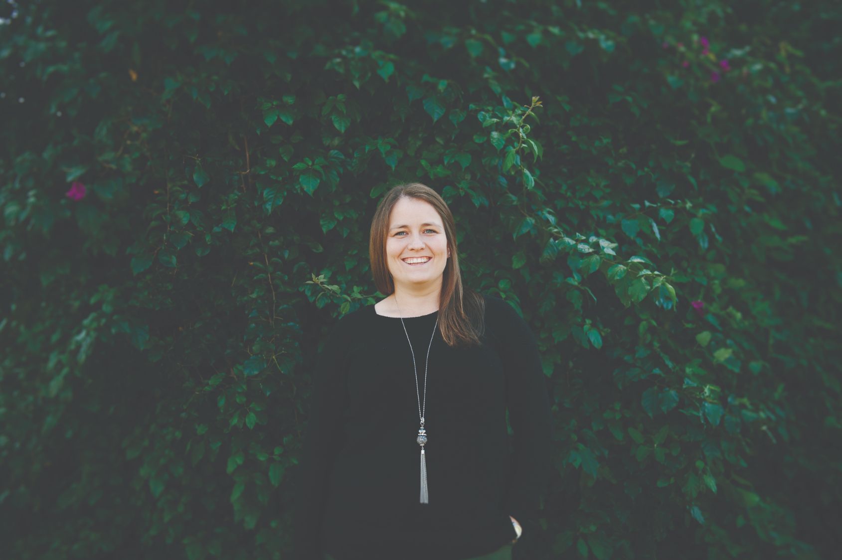 A woman in a black jumper standing in front of dense greenery