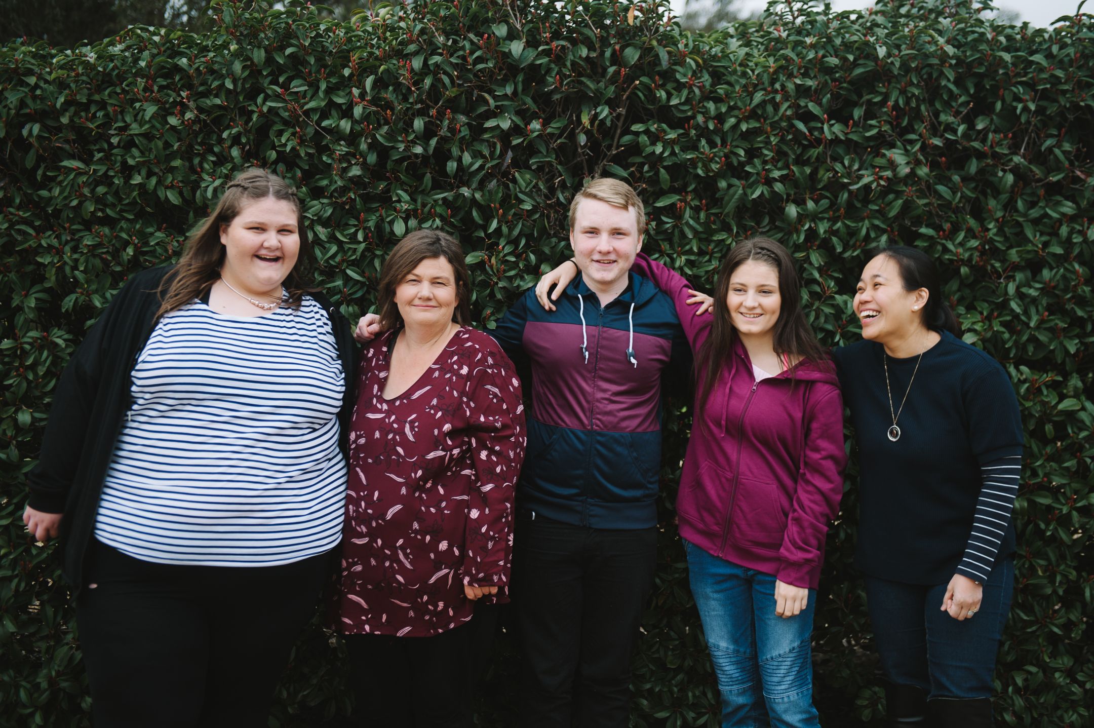 Dianne and her three children, and caseworker Jane, standing in front of tall foliage