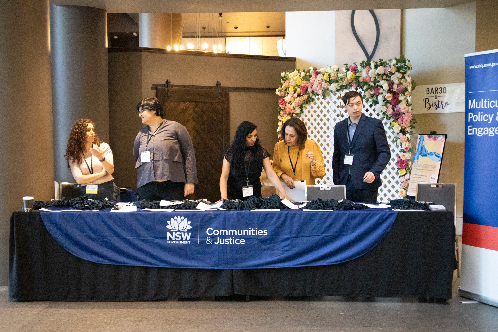 Five DCJ staff standing behind the conference registration table, talking to each other.