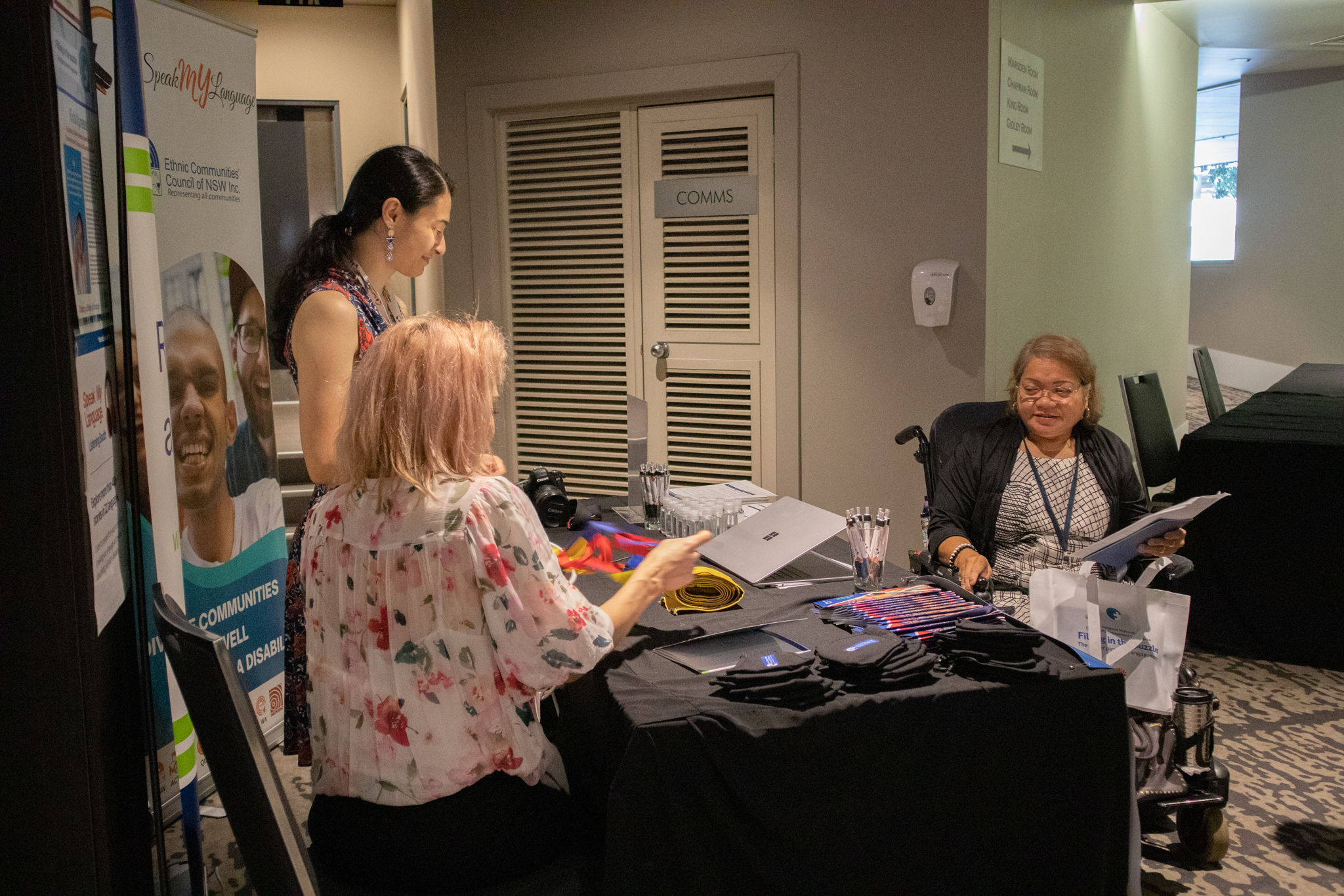 Two people behind a table smiling and talking to a person sitting on the other side of the table.