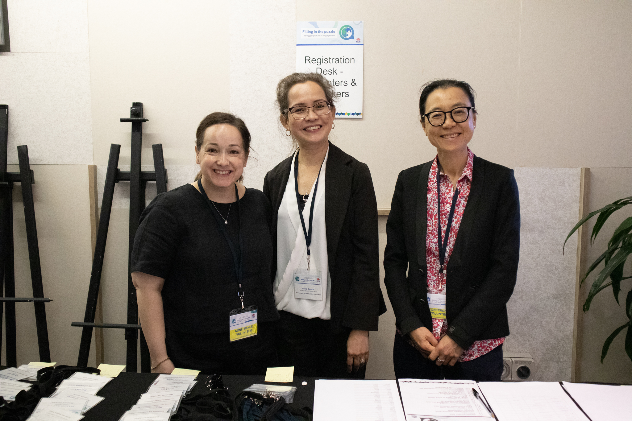 Three people standing behind a desk with registration papers