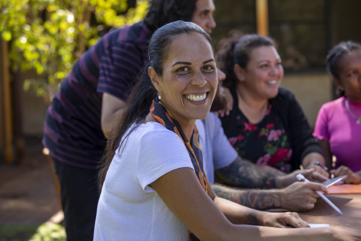 A group of  community workers meeting at an outdoor table. A woman in the foreground is smiling at the camera.